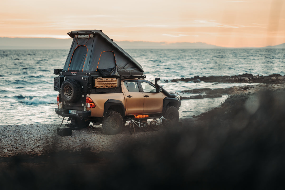 Alu-Cab Canopy Camper on a bronze Toyota Hilux parked on the coast, tent open