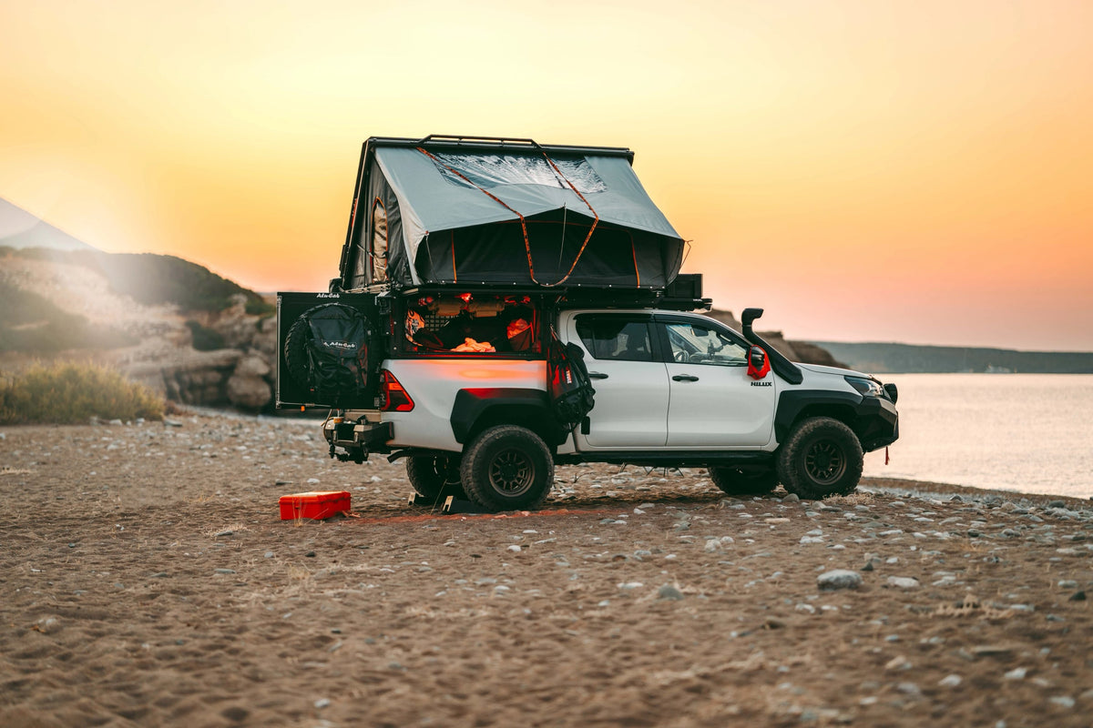 Alu-Cab ModCAP with Family tent open on a white Toyota Hilux double cab, parked on a beach at sunset