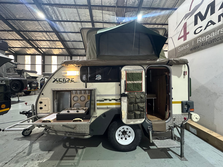 2010 Jurgens Xcape off-road caravan set up at camp with pop-top roof up, fold-out kitchen and entry door open — pre-owned unit at 4Matt Campers, Bellville Cape Town
