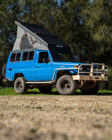 Alu-Cab Hercules black roof conversion open on a blue Land Cruiser Troopy